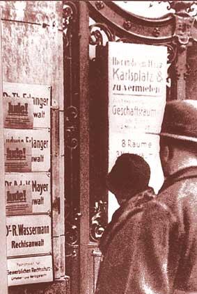 Ein Paar schauen am 1. April 1933 auf rote Handzettel, die auf Kanzleischilder geklebt wurden. Plakaten geklebt sind. SA-Posten fordern: „Geht nicht zu jüdischen Rechtsanwälten“; an die Kanzleischilder wurden rote Handzettel geklebt: „Besuch verboten! Jude!“