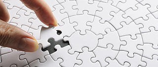 eine Hand fügt das letzte fehlende Puzzleteil ein